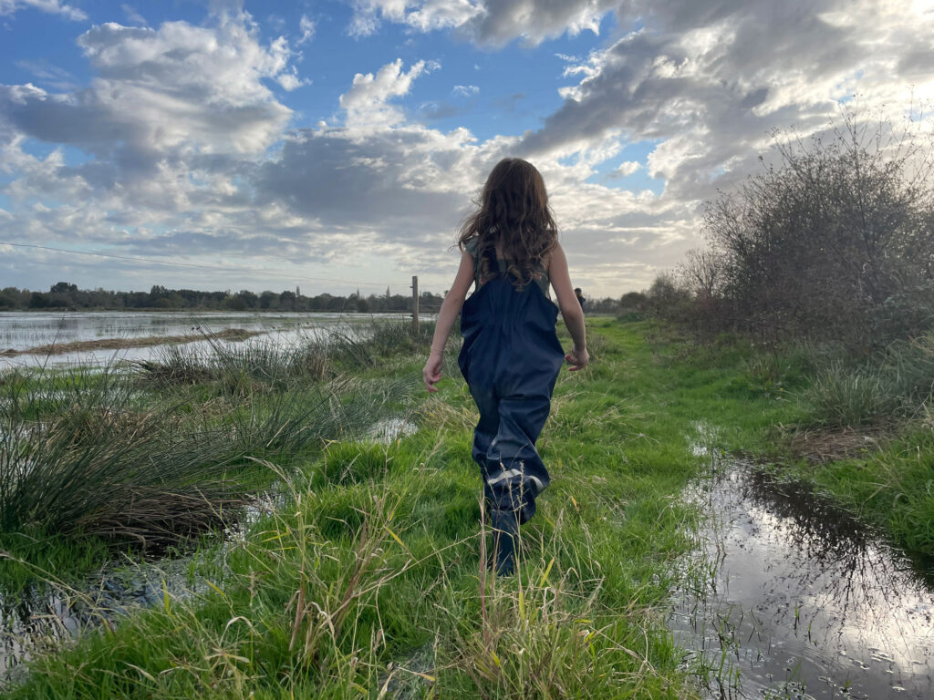 Jeune fille marchant dans un chemin de marais au bord d'une prairie humide inondée